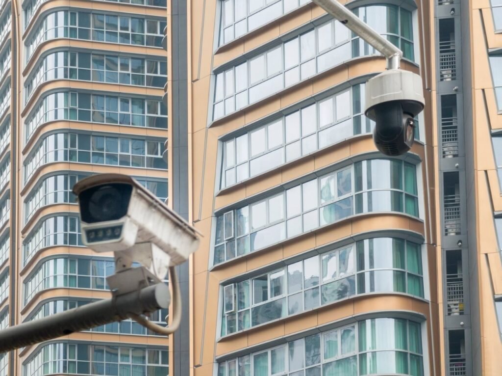 Two outdoor security cameras, including a bullet and a PTZ dome, mounted on poles against a backdrop of modern high-rise buildings, representing the urban infrastructure factors to consider when calculating CCTV installation costs in Singapore for a professional cctv installation or security camera installation.