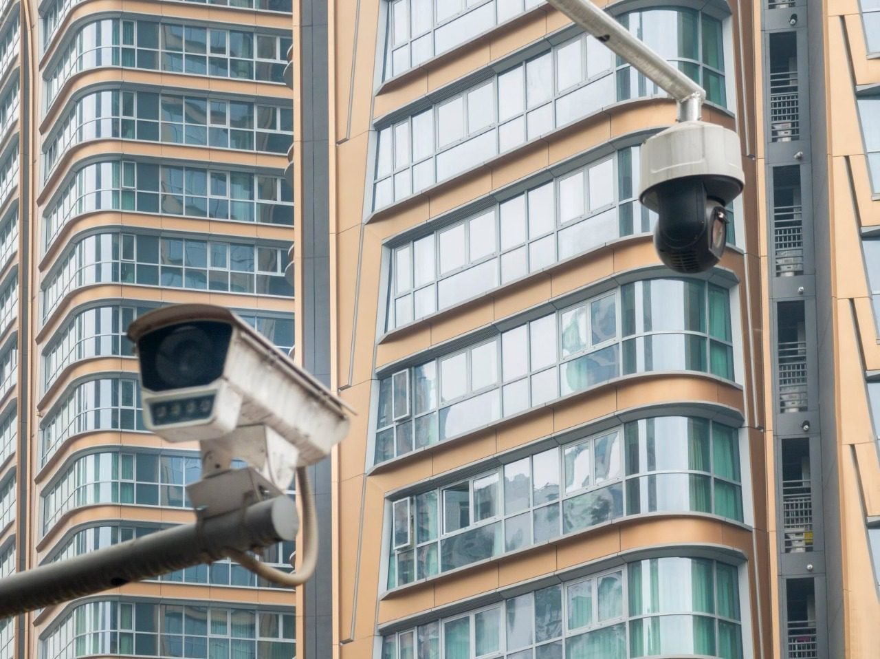Two outdoor security cameras, including a bullet and a PTZ dome, mounted on poles against a backdrop of modern high-rise buildings, representing the urban infrastructure factors to consider when calculating CCTV installation costs in Singapore for a professional cctv installation or security camera installation.